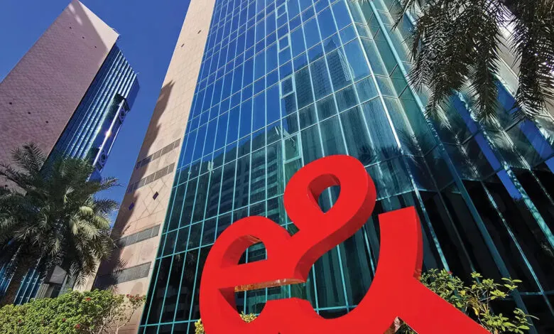 Large red 'e&' logo in front of modern glass skyscrapers under a clear blue sky.