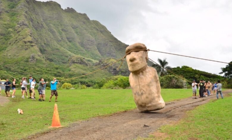 A group of people pulling a replica Moai statue with ropes across a grassy field.