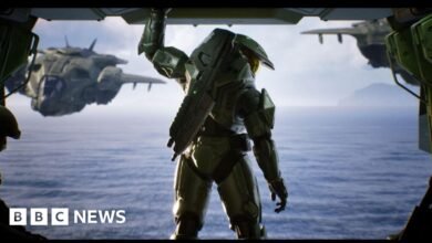 Master Chief in his iconic green armor stands ready, looking out at a vast ocean with a Pelican dropship in the background.