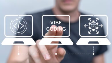 A person's hand touches a virtual screen displaying 'VIBE CODING' between two laptops with coding icons.