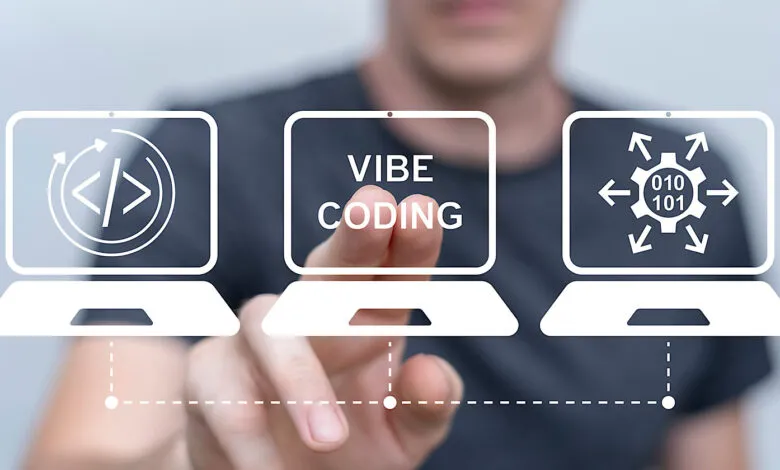 A person's hand touches a virtual screen displaying 'VIBE CODING' between two laptops with coding icons.