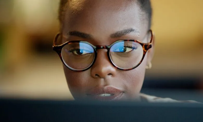Close-up of a Black woman wearing glasses, focused on a computer screen.