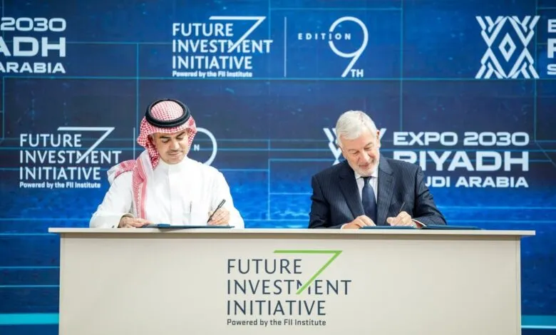 Two men signing documents at a table with Future Investment Initiative branding.
