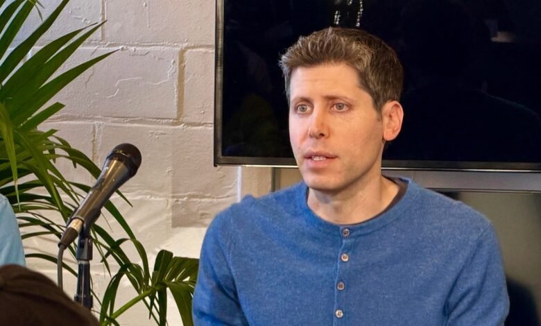 Man in blue shirt speaking into a microphone with plants and a screen in the background.