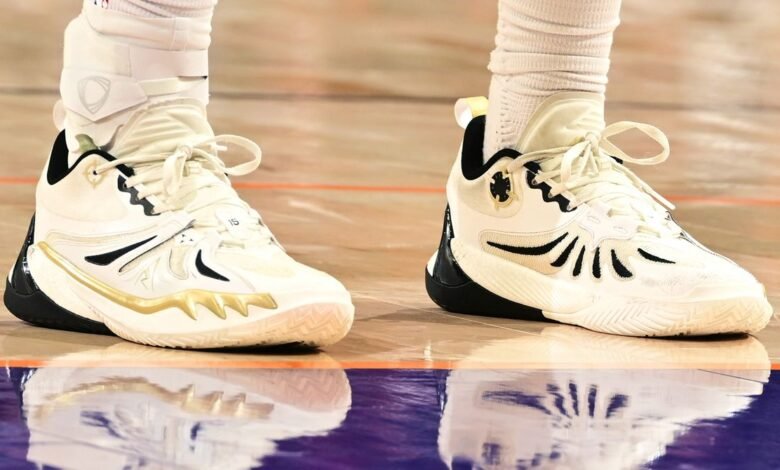 Close-up of a basketball player's white and gold sneakers with ankle braces on a polished court.