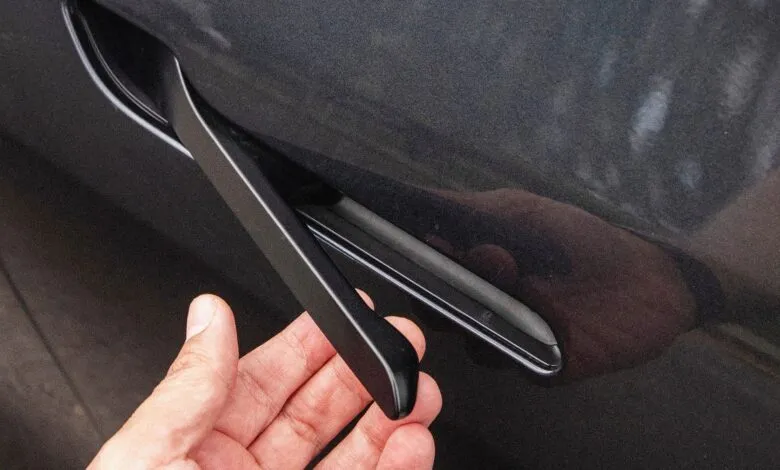 Close-up of a hand reaching for a flush car door handle.