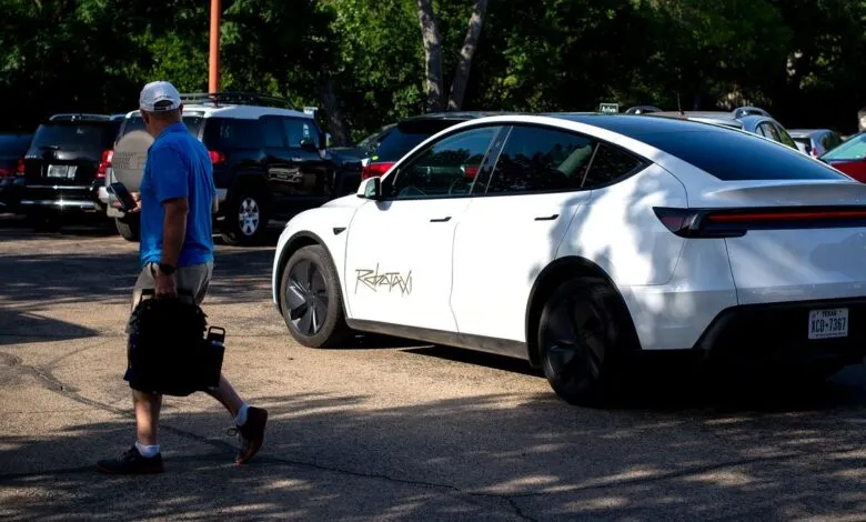 Man walks past a white Tesla Robotaxi with a distinctive gold decal on its side.