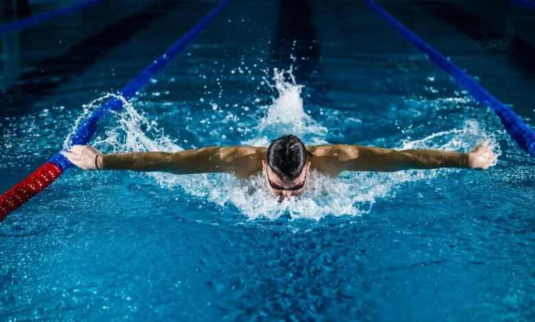 Swimmer performing the butterfly stroke in a competition pool, creating a large splash.