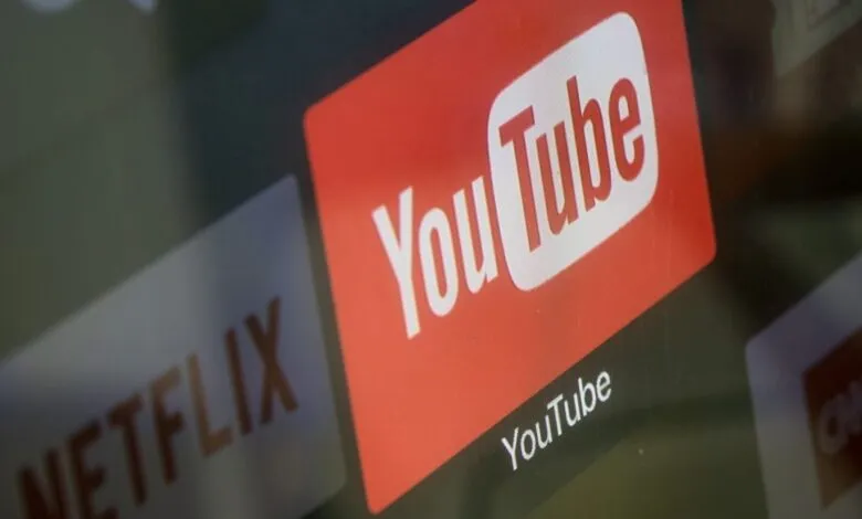 Close-up of the YouTube logo on a screen, with Netflix and CNN logos blurred in the background.