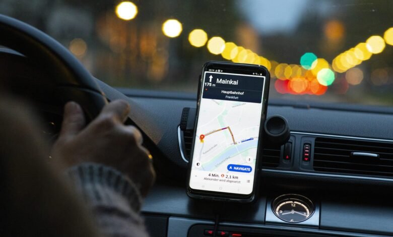 Person driving at night, using a smartphone navigation app showing directions to Mainkai, Frankfurt.