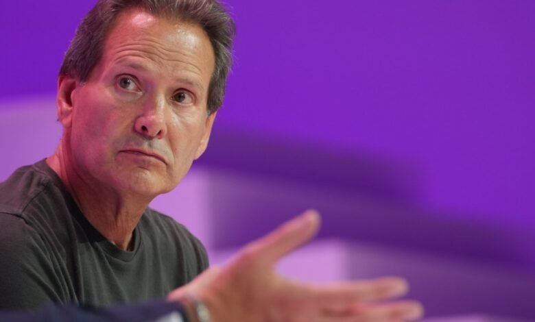 Close-up of a man with graying hair and a dark t-shirt, looking off to the side with a thoughtful expression.
