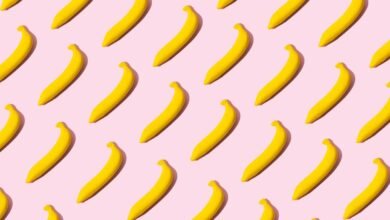 A repeating pattern of bright yellow bananas on a pastel pink background.