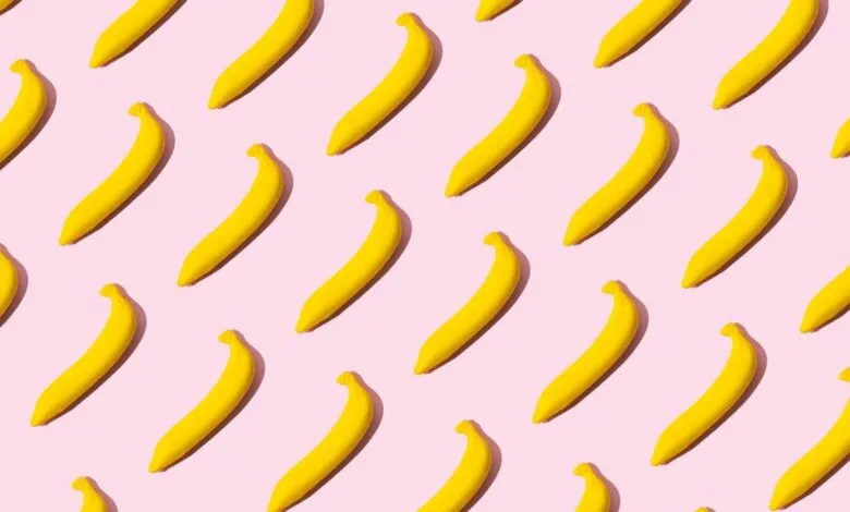 A repeating pattern of bright yellow bananas on a pastel pink background.