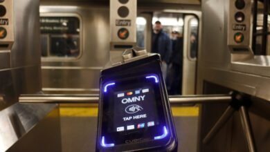 OMNY contactless payment reader at a subway turnstile with a train in the background.