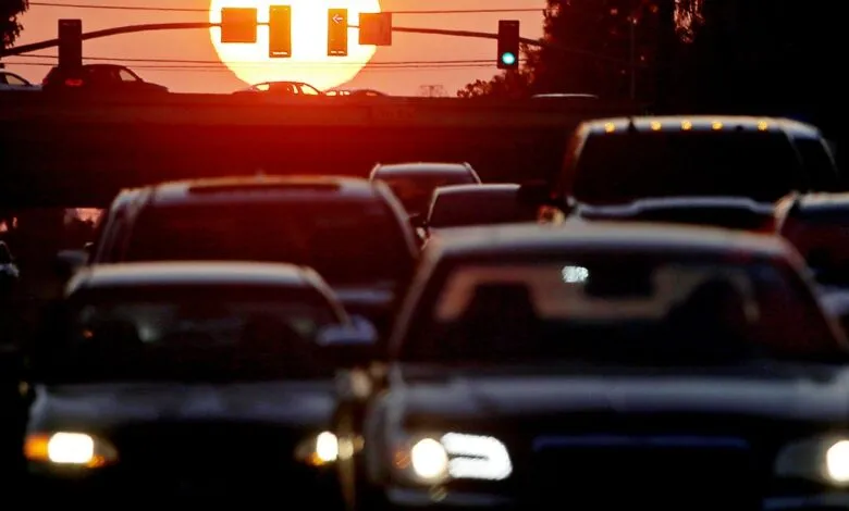 Cars in traffic at sunset with a large sun and traffic lights.