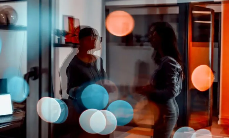 Two women in silhouette talking in a modern office with bokeh lights.