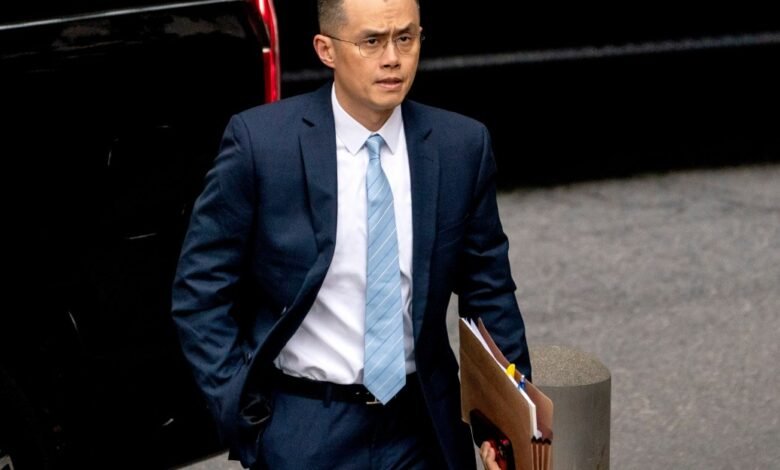 Changpeng Zhao, CEO of Binance, walks with documents in a suit.