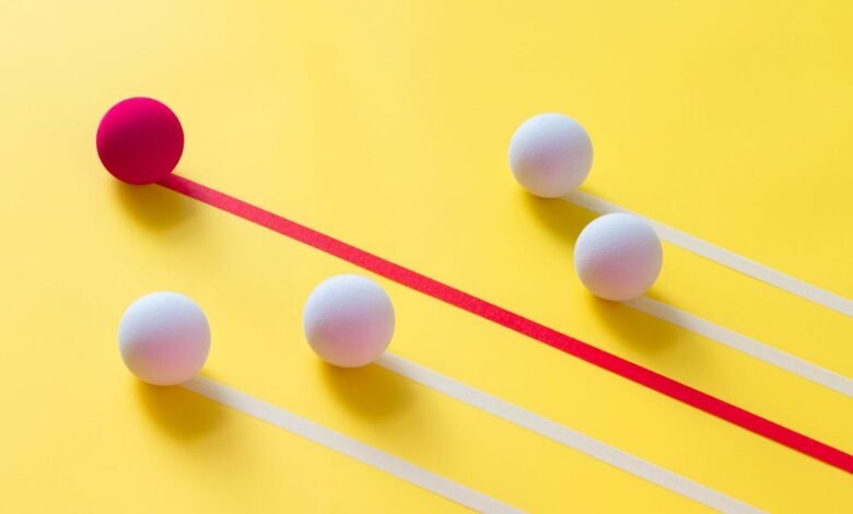 A single pink sphere leads a line of white spheres on a bright yellow background.
