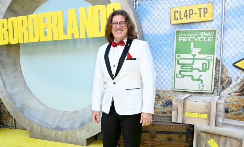 Man in a white tuxedo with a red bowtie smiles at a Borderlands movie premiere.