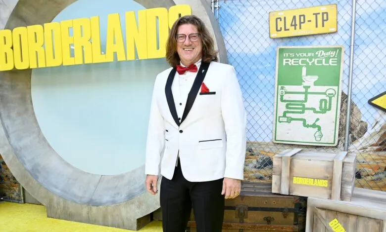 Man in a white tuxedo with a red bowtie smiles at a Borderlands movie premiere.