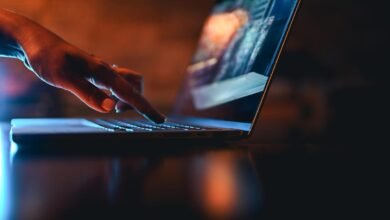 Close-up of a hand using a laptop with blue and orange lighting.