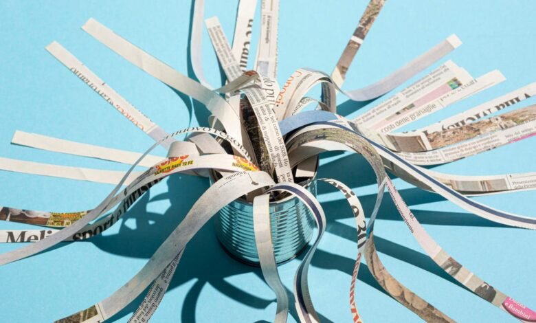 Shredded newspaper strips emerging from a tin can against a blue background.