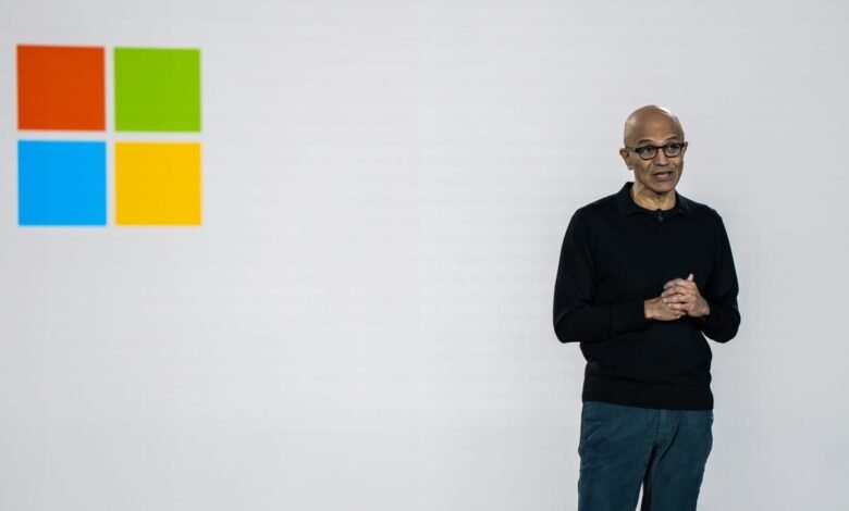 Satya Nadella stands before the Microsoft logo during a presentation.