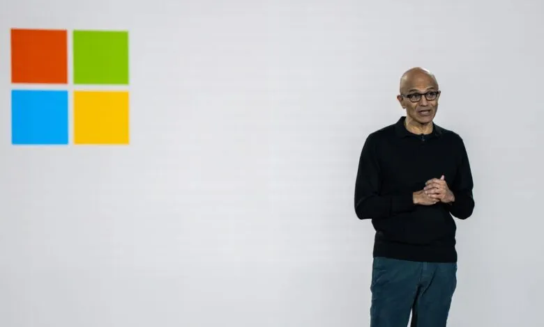 Satya Nadella stands before the Microsoft logo during a presentation.