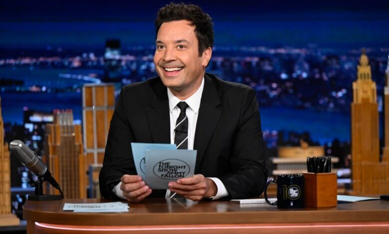 Jimmy Fallon smiles while holding cue cards on The Tonight Show set.