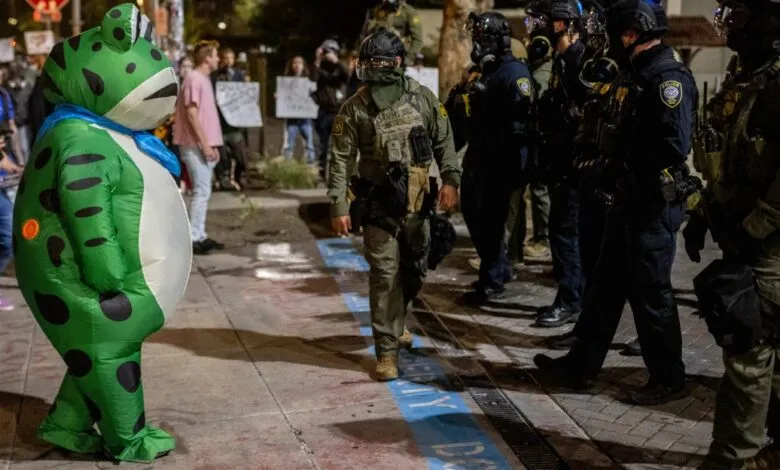 Inflatable frog costume stands opposite a line of law enforcement officers in tactical gear.