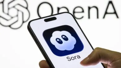 Close-up of a smartphone displaying the Sora app icon, with the OpenAI logo blurred in the background.