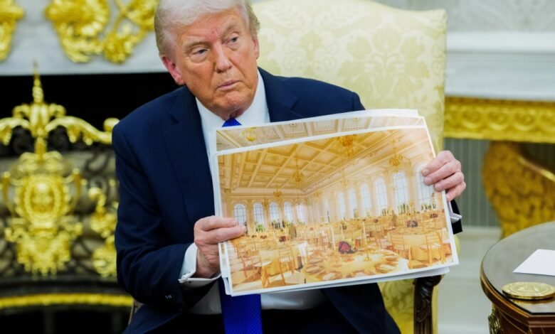Donald Trump holds up a photograph of a grand ballroom set for a formal event.
