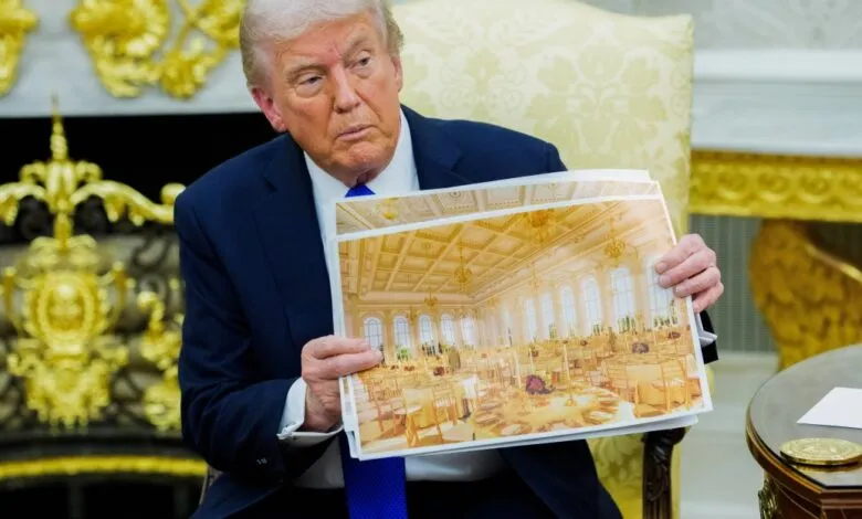 Donald Trump holds up a photograph of a grand ballroom set for a formal event.