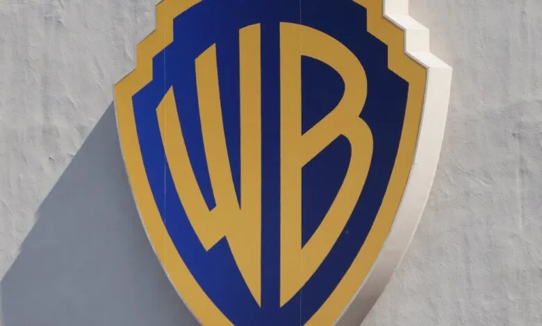 Close-up of the Warner Bros. shield logo in blue and gold against a textured white wall.