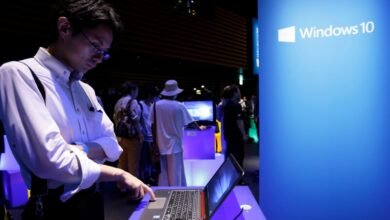 Man using a laptop at a Windows 10 event with a large blue banner.