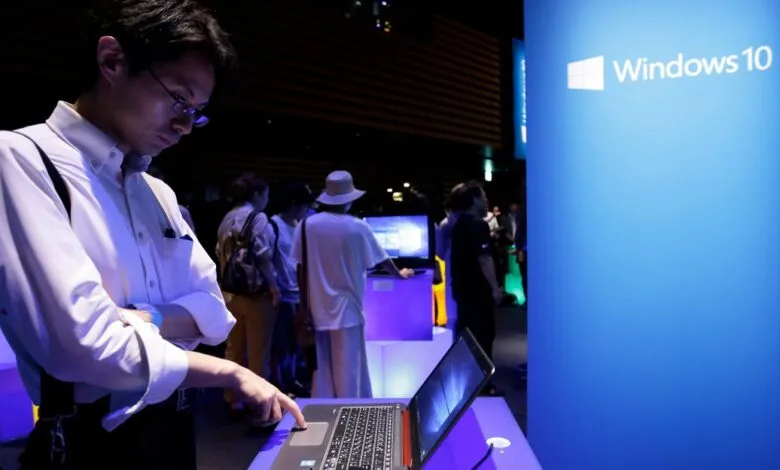 Man using a laptop at a Windows 10 event with a large blue banner.