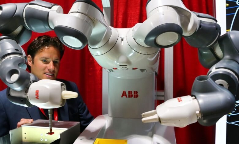 Man in suit interacting with a white and gray robotic arm with ABB logo.