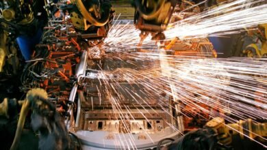 Robotic arms welding a car chassis, creating a shower of bright orange sparks.