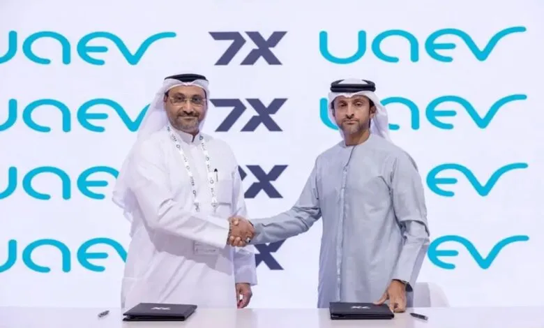 Two men in traditional Arab attire shaking hands in front of a backdrop with logos.