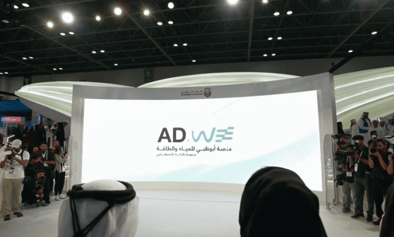 Large screen displaying ADwE logo and Arabic text, with people watching.