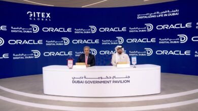 Two men in formal attire sit at a table in front of a backdrop with Oracle and Gitex Global logos.