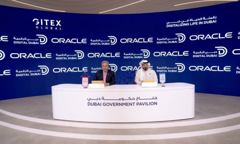 Two men in formal attire sit at a table in front of a backdrop with Oracle and Gitex Global logos.