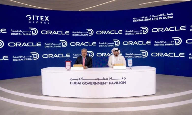 Two men in formal attire sit at a table in front of a backdrop with Oracle and Gitex Global logos.