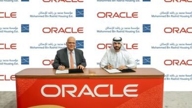 Two men signing documents at a table with Oracle branding.