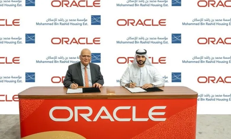 Two men signing documents at a table with Oracle branding.