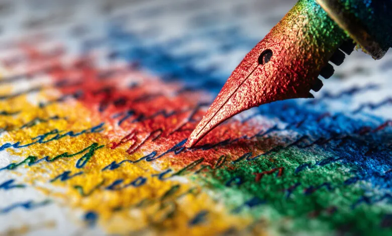 Close-up of a rainbow-colored fountain pen nib writing on textured paper with colorful ink.