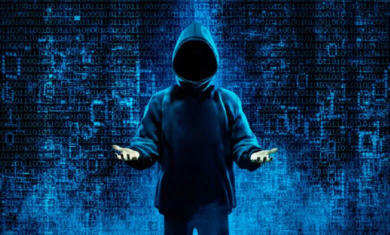 Anonymous hacker in a blue hoodie with hands outstretched against a backdrop of glowing blue binary code.