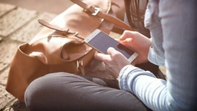 Person using a smartphone next to a brown leather backpack.