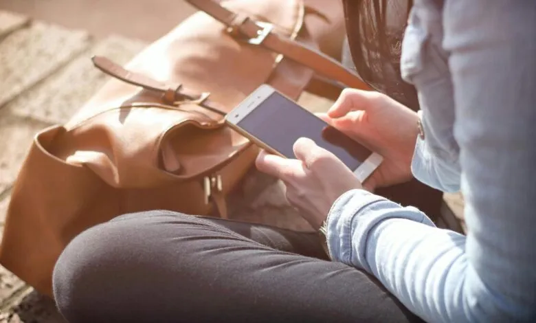 Person using a smartphone next to a brown leather backpack.