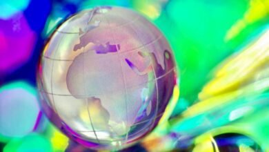 Close-up of a glass globe with continents etched on its surface, set against a vibrant, blurred background of colorful lights.